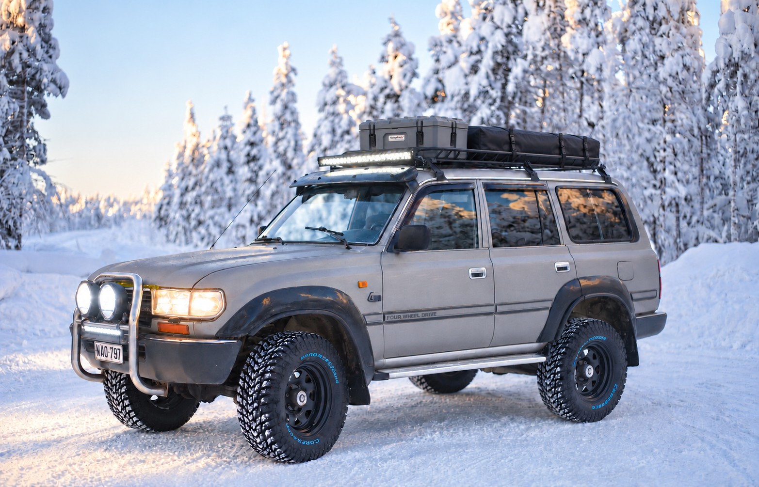 Our 1992 Toyota Land Cruiser HDJ80 with a grey Terrafirma roof box, a long black tent bag and illuminated driving lights on a snowy forest road